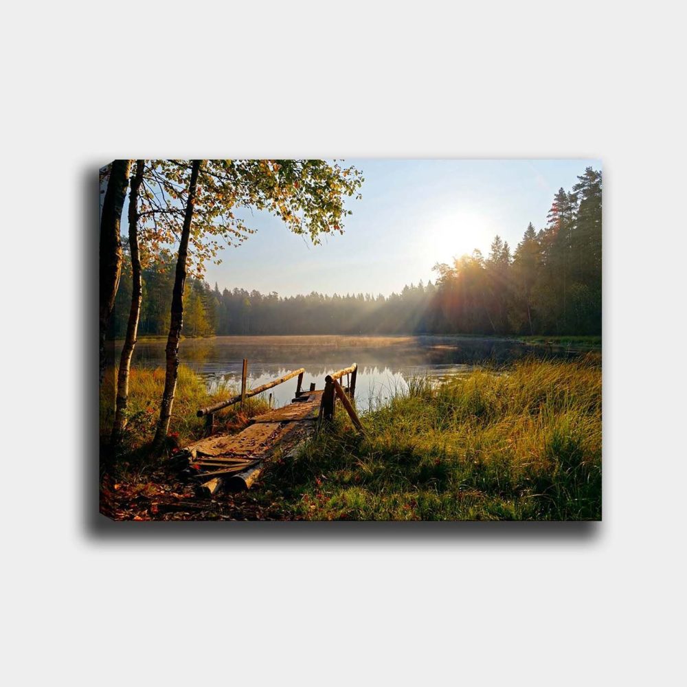 Canvastavla 70x100 cm - Stilla sjö med en träbro omgiven av grönskande träd och morgonsolens strålar